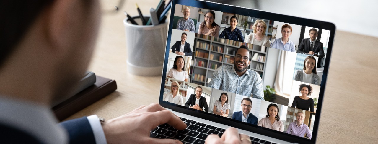 Man taking a virtual call for work with a dozen faces on the screen. Photo/UC Marketing+Communications